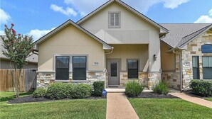 A two-story house with a beige exterior, stone accents, and a front entrance.