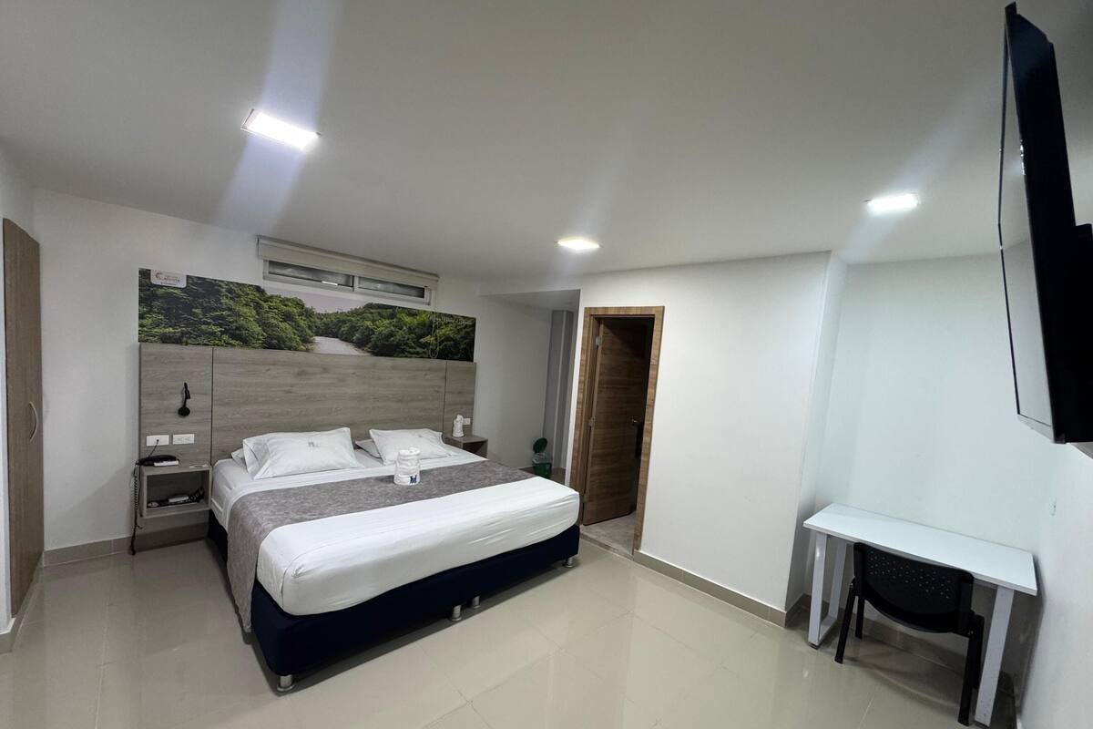 A modern hotel room with a large bed, a desk, and a TV.