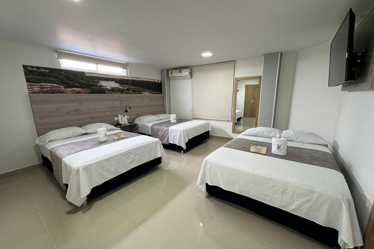 A hotel room with three beds, a large mirror, and a painting of a landscape.