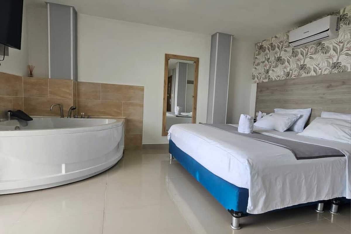 A modern hotel room with a large bathtub, a double bed, and a wooden headboard.