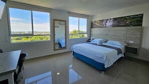 Un dormitorio moderno con una cama grande, un escritorio y vistas a zonas verdes a través de las ventanas.