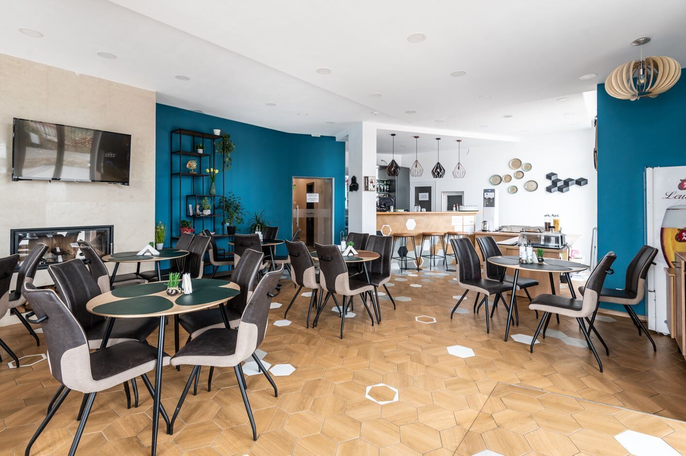 A modern restaurant with hexagonal patterned flooring, black and gray chairs, and a blue accent wall.