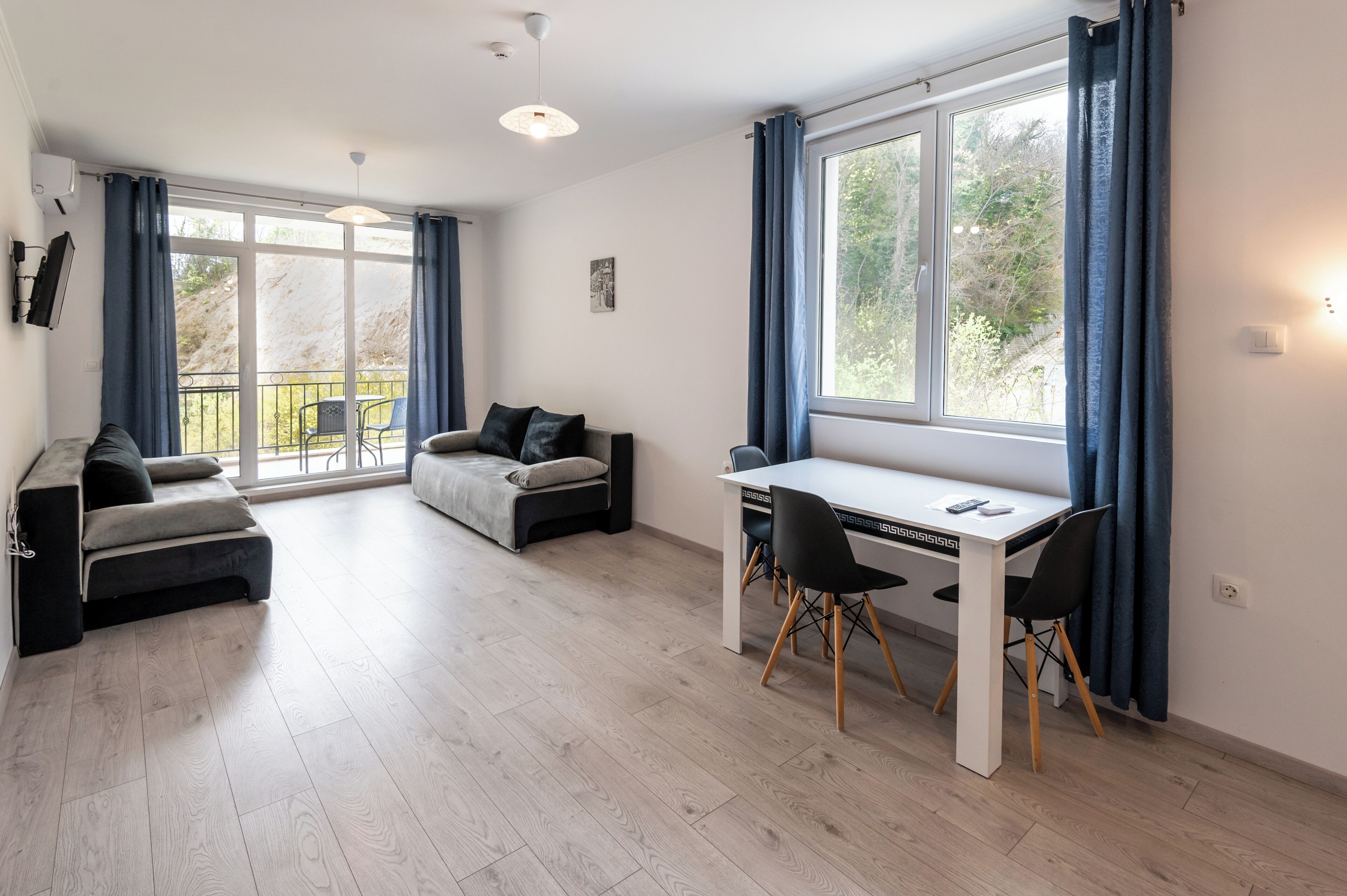 Een moderne woonkamer met een bank, een eettafel met stoelen en een groot raam met gordijnen.