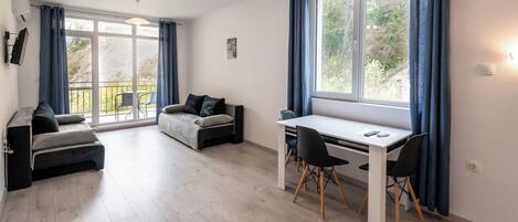 Een moderne woonkamer met een bank, een eettafel met stoelen en een groot raam met gordijnen.