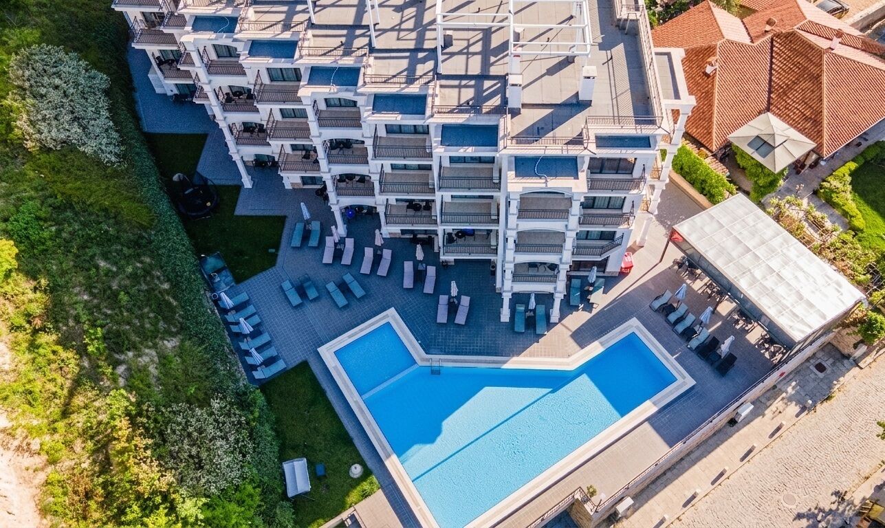 Ein Luftbild eines Hotels mit mehreren Balkonen, einem Schwimmbecken und Liegebereichen.