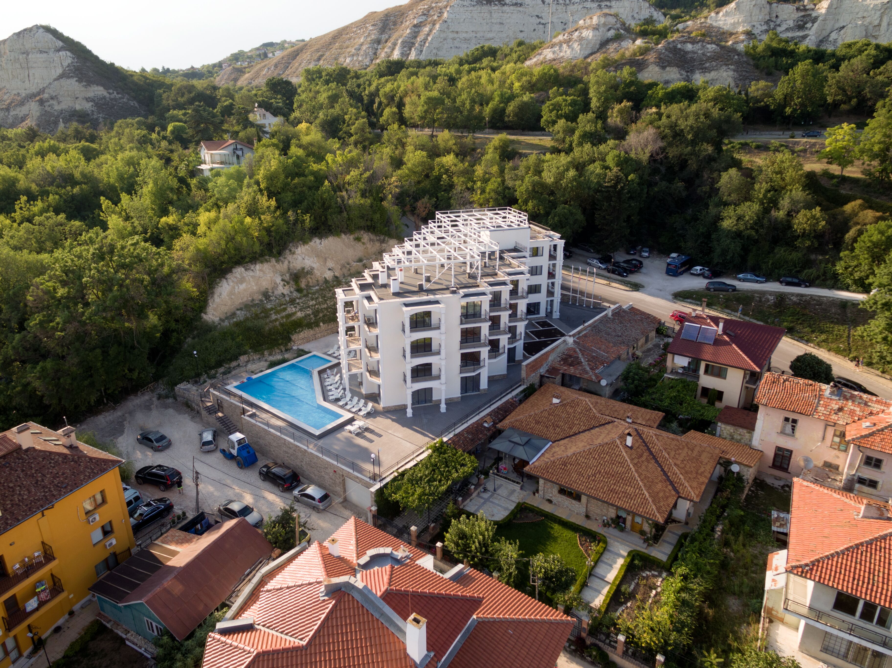Un hotel moderno con piscina en la azotea, rodeado de exuberante vegetación y montañas al fondo.
