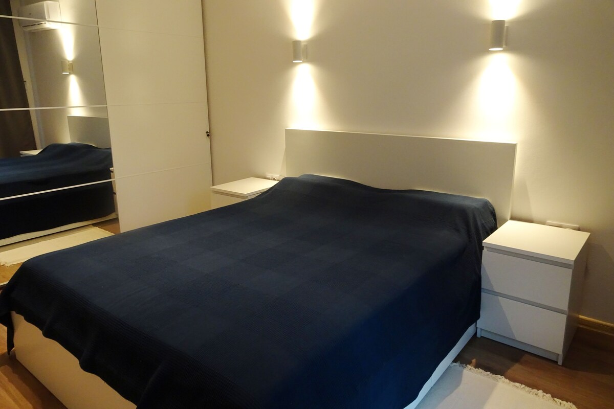 Ein Schlafzimmer mit Bett, Nachttischen, einem Kleiderschrank und Wandleuchten.