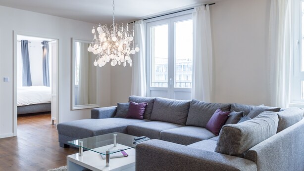 A modern living room with a grey sectional sofa, a glass coffee table, and a chandelier. - Exclusive backyard loft, quiet, in HH-Uhlenhorst, car parkling space possible (Hamburg)