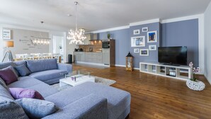 A modern living room with a grey sectional sofa, a flat-screen TV, wooden flooring, and a kitchen in the background. - Exclusive backyard loft, quiet, in HH-Uhlenhorst, car parkling space possible (Hamburg)