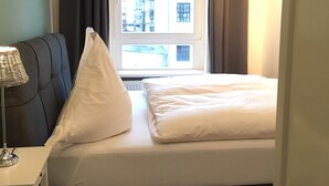 A bedroom with a bed, a bedside table, a lamp, and a window with curtains. - Exclusive backyard loft, quiet, in HH-Uhlenhorst, car parkling space possible (Hamburg)