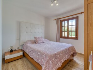 A bedroom with a bed, a bedside table, a lamp, and a window with curtains.