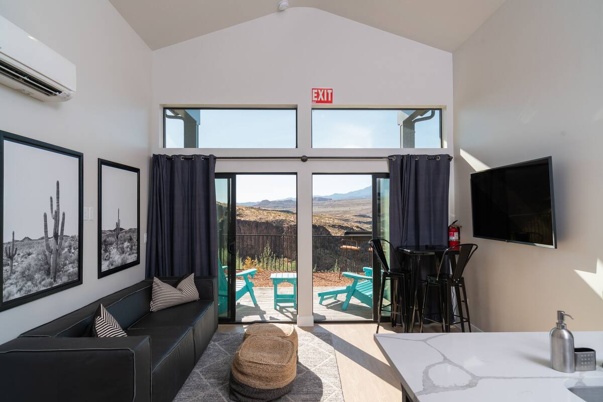 A modern hotel room with a large sliding glass door leading to an outdoor patio with green furniture and a scenic view.