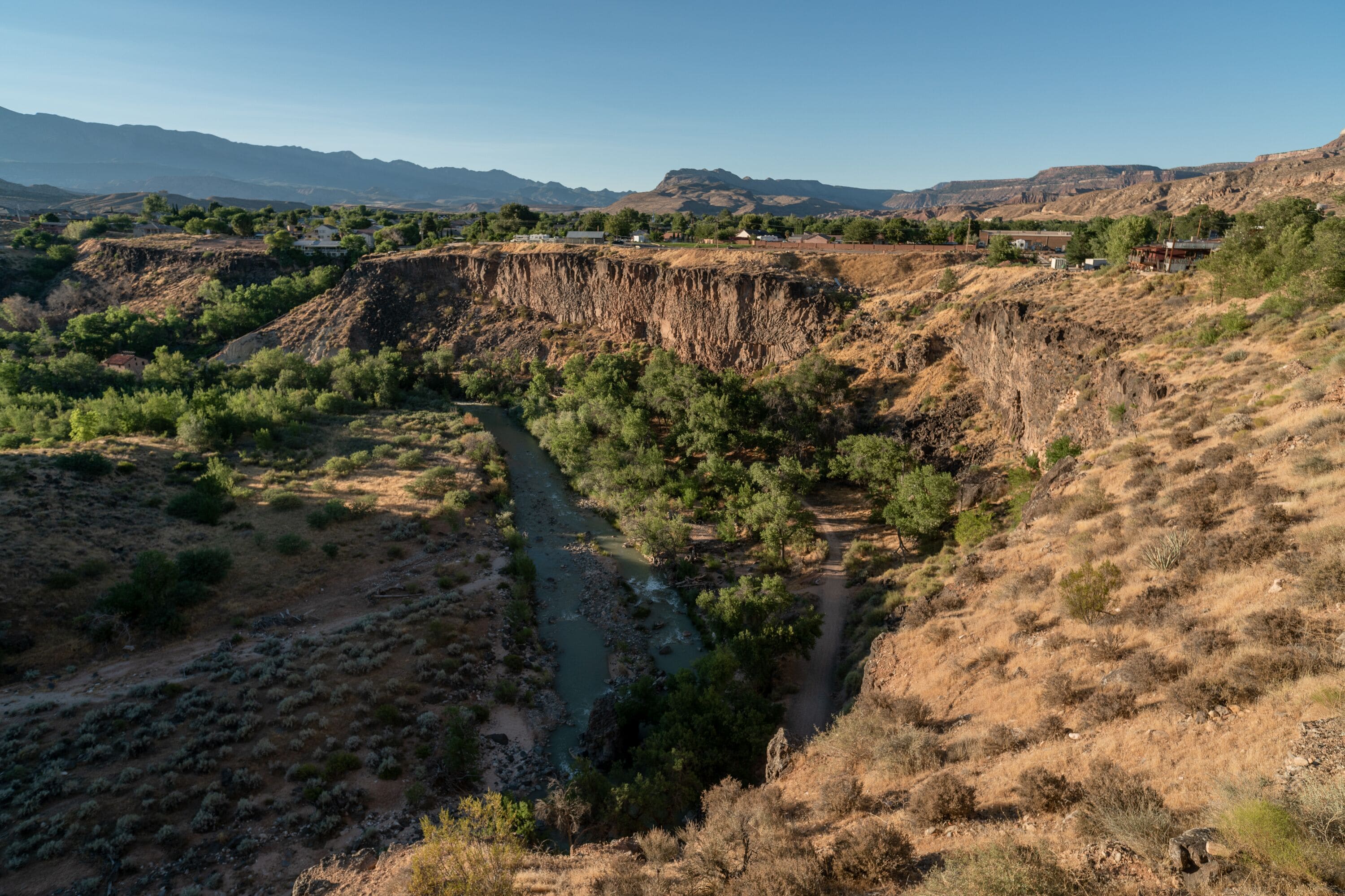 A canyon landscape with a river, sparse vegetation, and distant mountains.