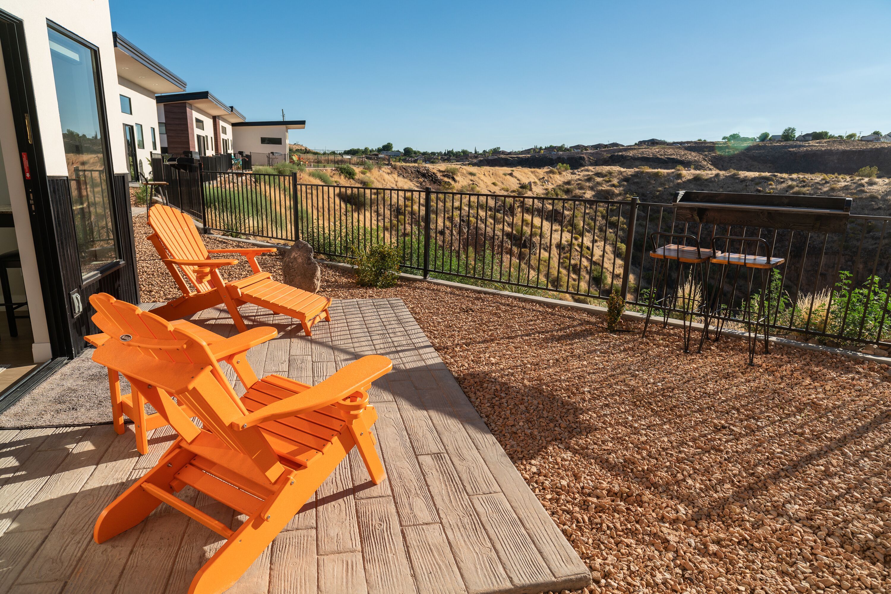 A deck with orange chairs and a table, overlooking a hilly landscape.
