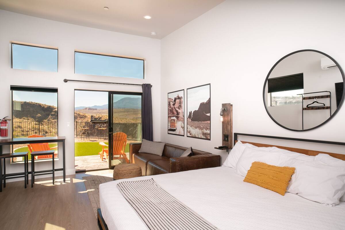 A spacious bedroom with a large bed, a desk, and a balcony with a view of the mountains.