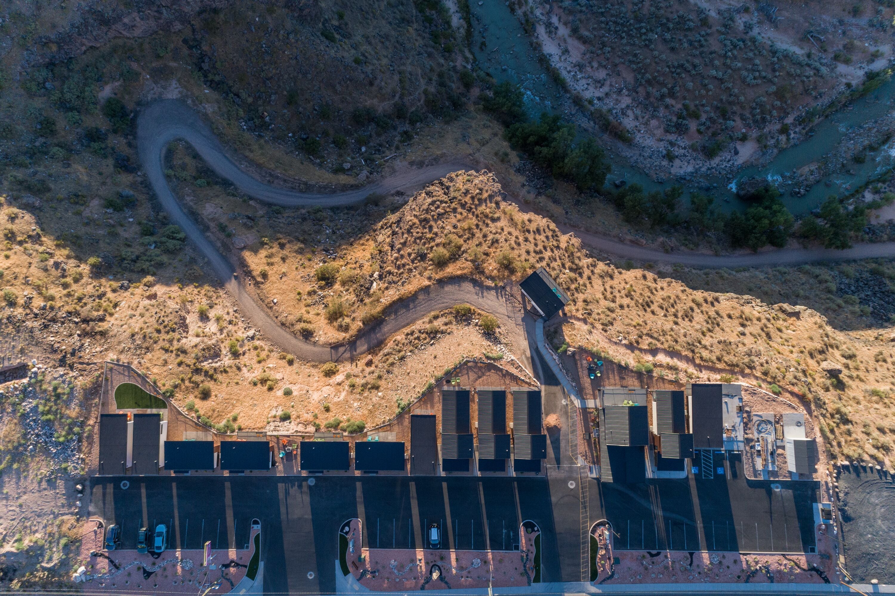 An aerial view of a building with a parking lot, surrounded by a hilly landscape.