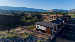 A modern building with a flat roof, surrounded by a parking lot and a mountainous landscape. - The Dwellings (La Verkin)