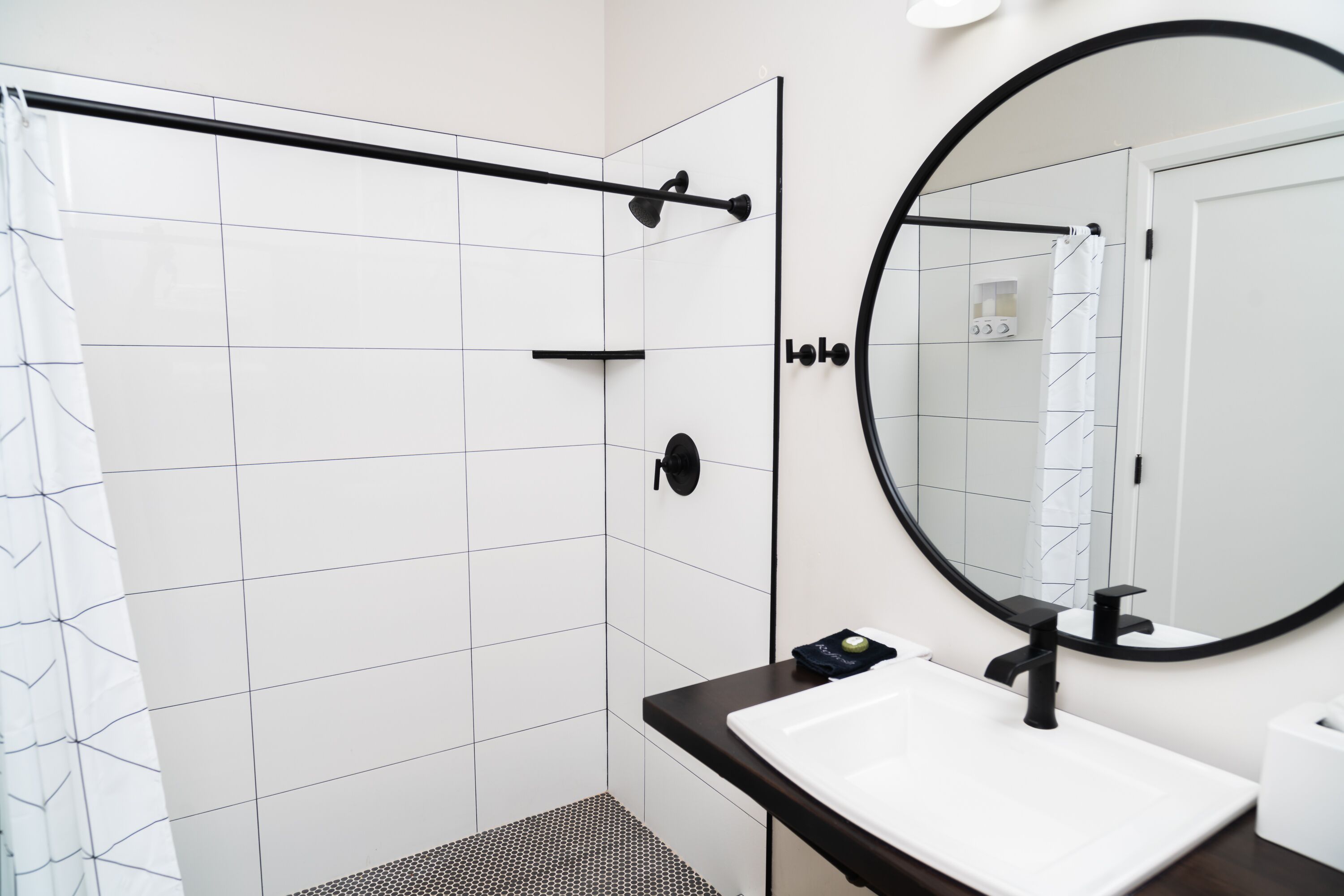 A modern bathroom with a shower, a white sink, a black faucet, and a large mirror.