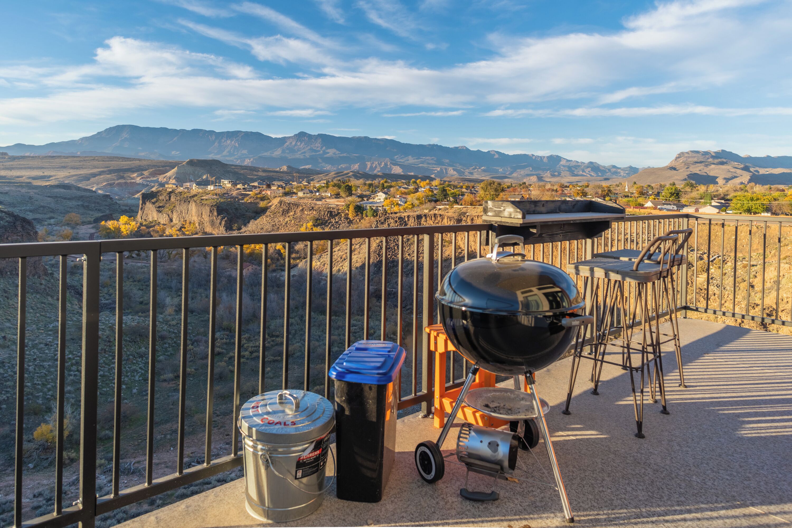 A balcony with a barbecue setup, including a grill, chairs, and trash bins.