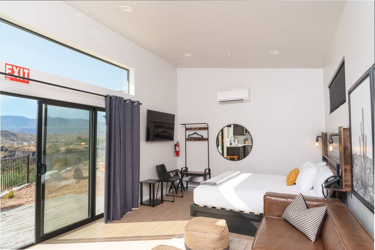 A modern hotel room with a bed, a seating area, a desk, and a large window offering a scenic view.