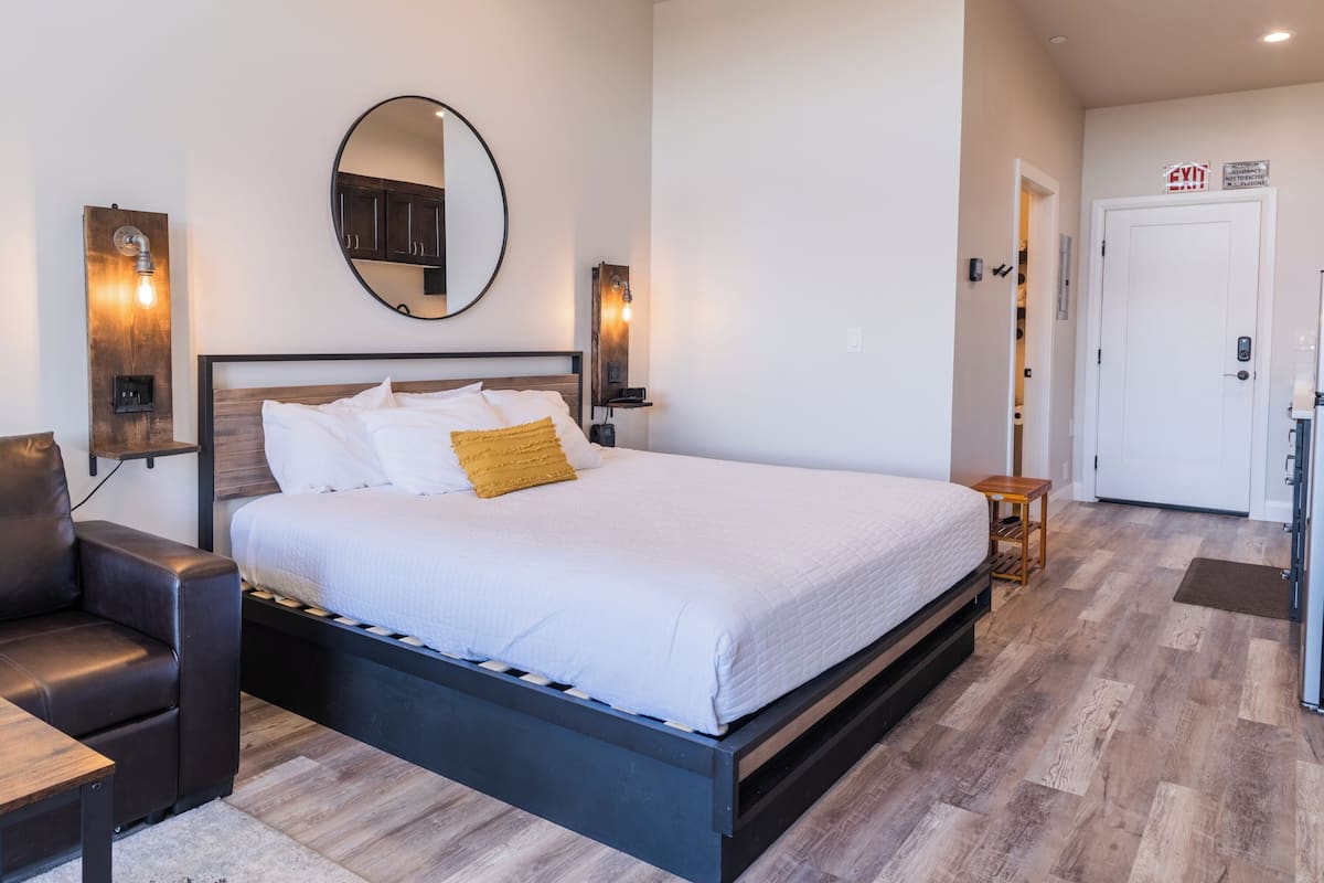 A modern hotel room with a large bed, a round mirror, and two wall-mounted light fixtures.