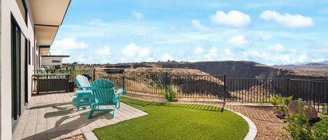 A balcony with a view of a hilly landscape, a small lawn, and two chairs.