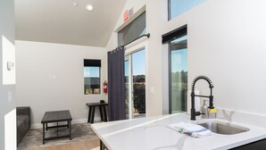 A modern kitchen with a white countertop, a built-in sink, and a window overlooking a balcony. - The Dwellings (La Verkin)
