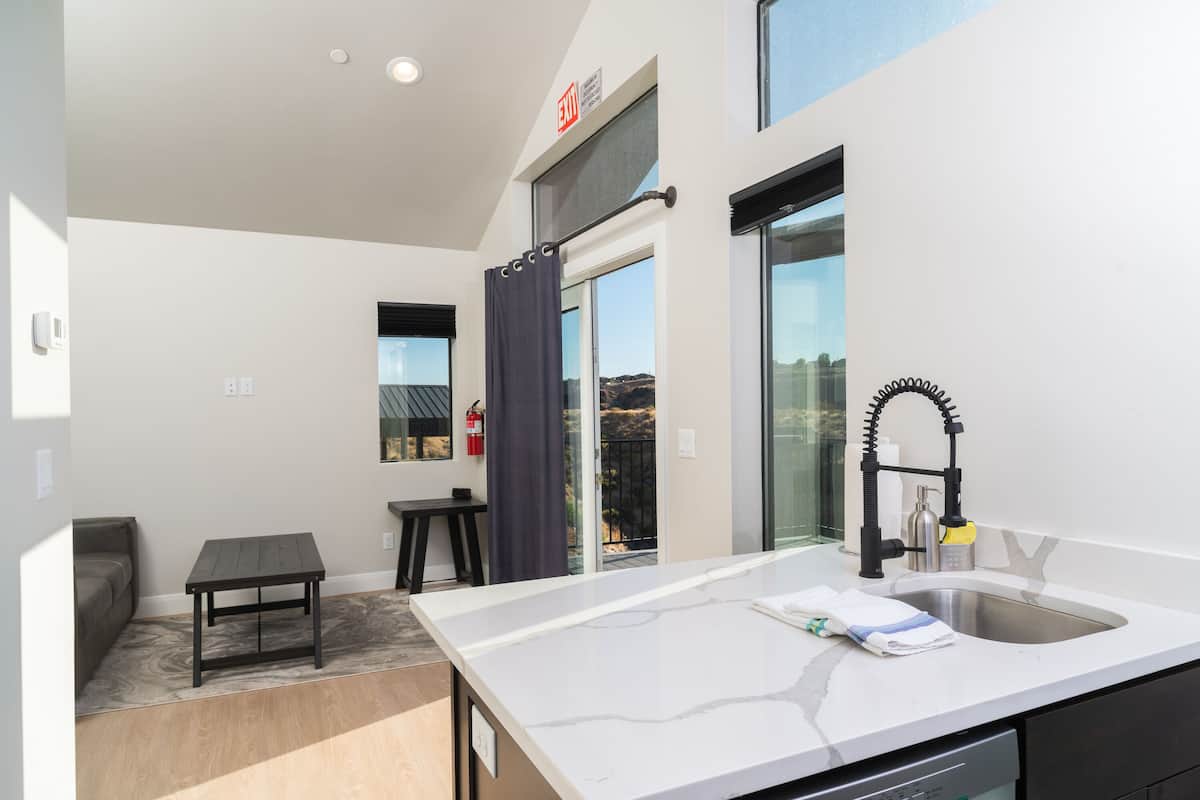 A modern kitchen with a white countertop, a built-in sink, and a window overlooking a balcony.