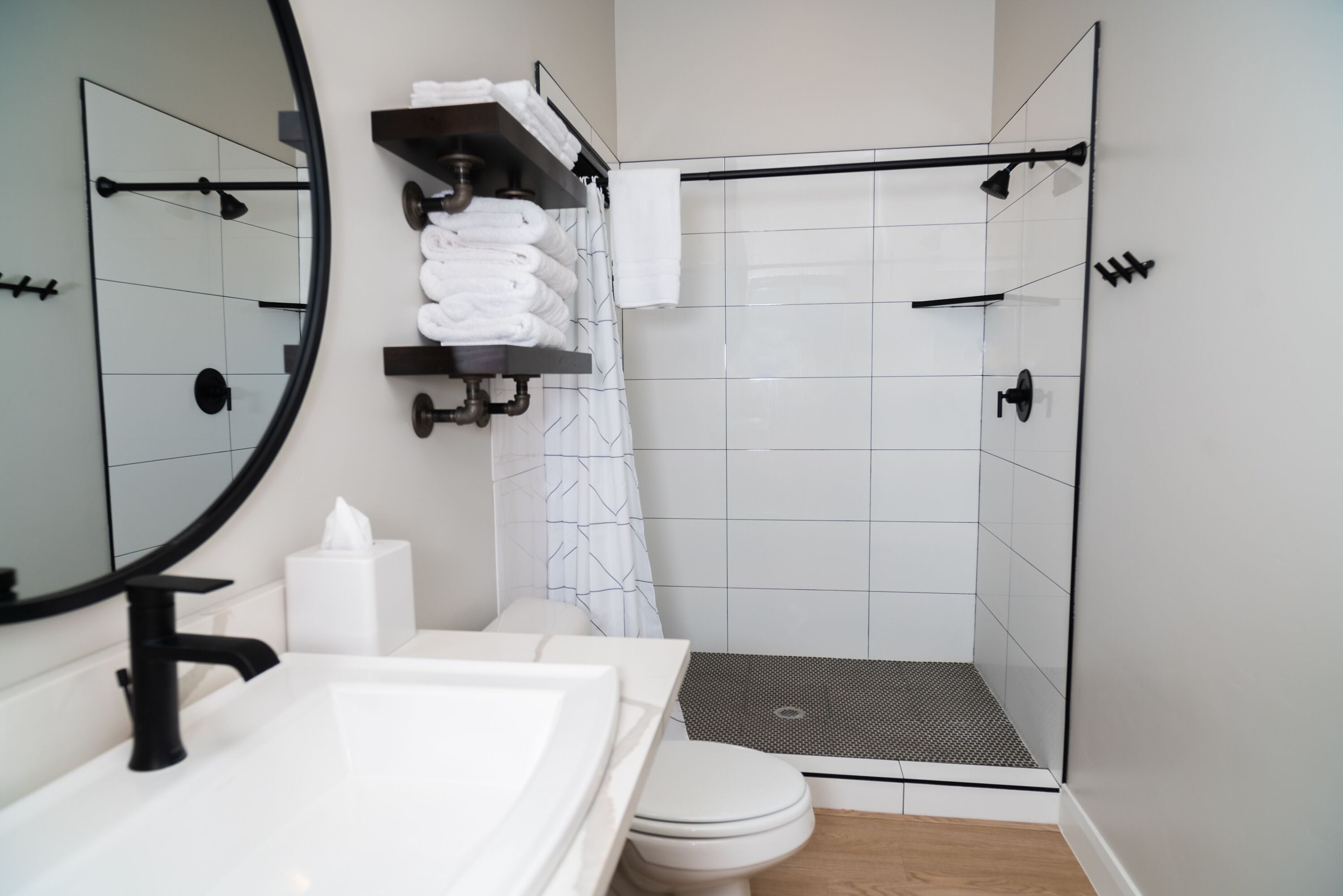 A modern bathroom with a white sink, a toilet, a shower with a black floor, and a towel rack with folded towels.