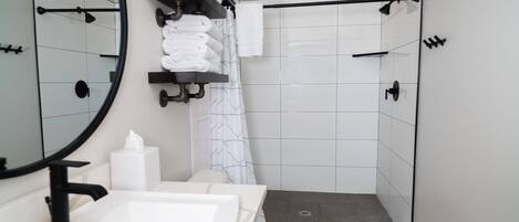 A modern bathroom with a white sink, a toilet, a shower with a black floor, and a towel rack with folded towels.