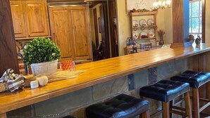 Une cuisine avec des meubles de rangement en bois, un îlot central doté de tabourets, un éclairage suspendu et une étagère décorative fixée au mur.