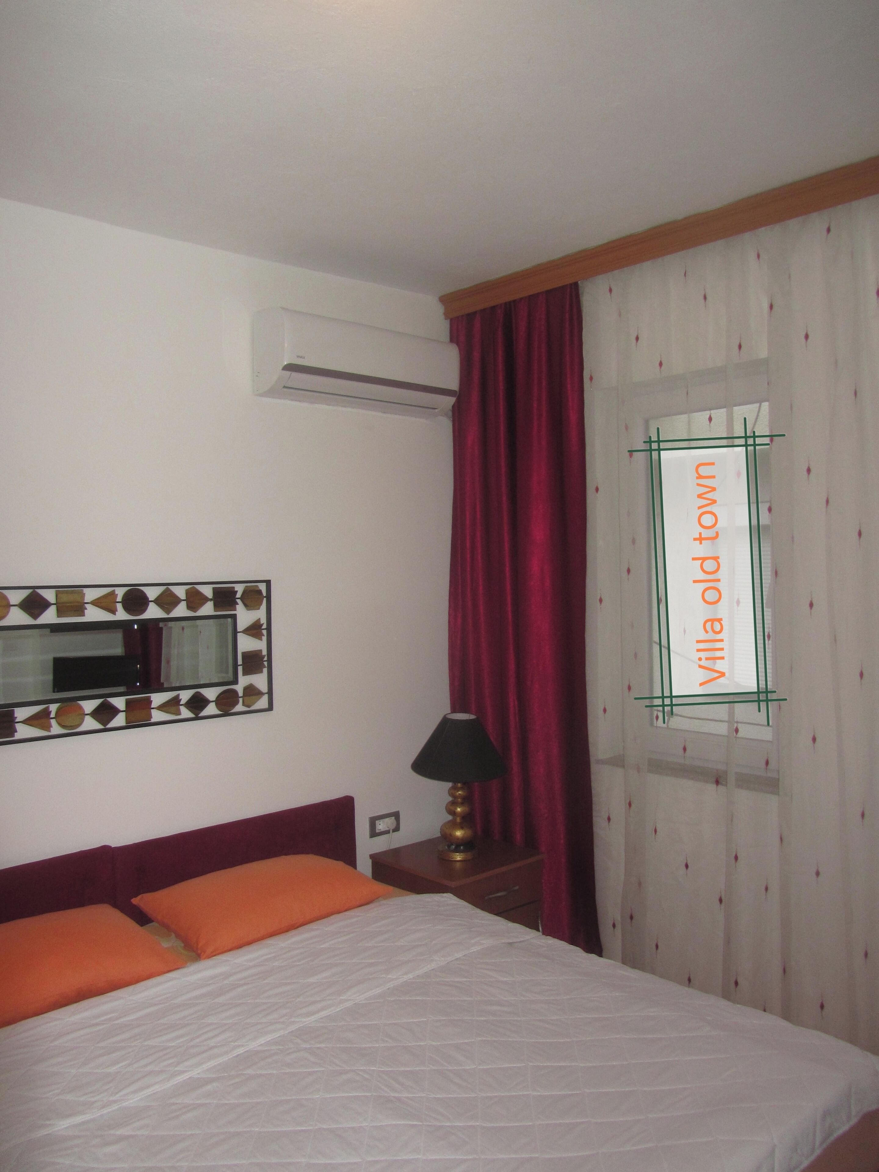 A hotel room with a bed, a nightstand, a lamp, an air conditioning unit, and a window with a curtain.