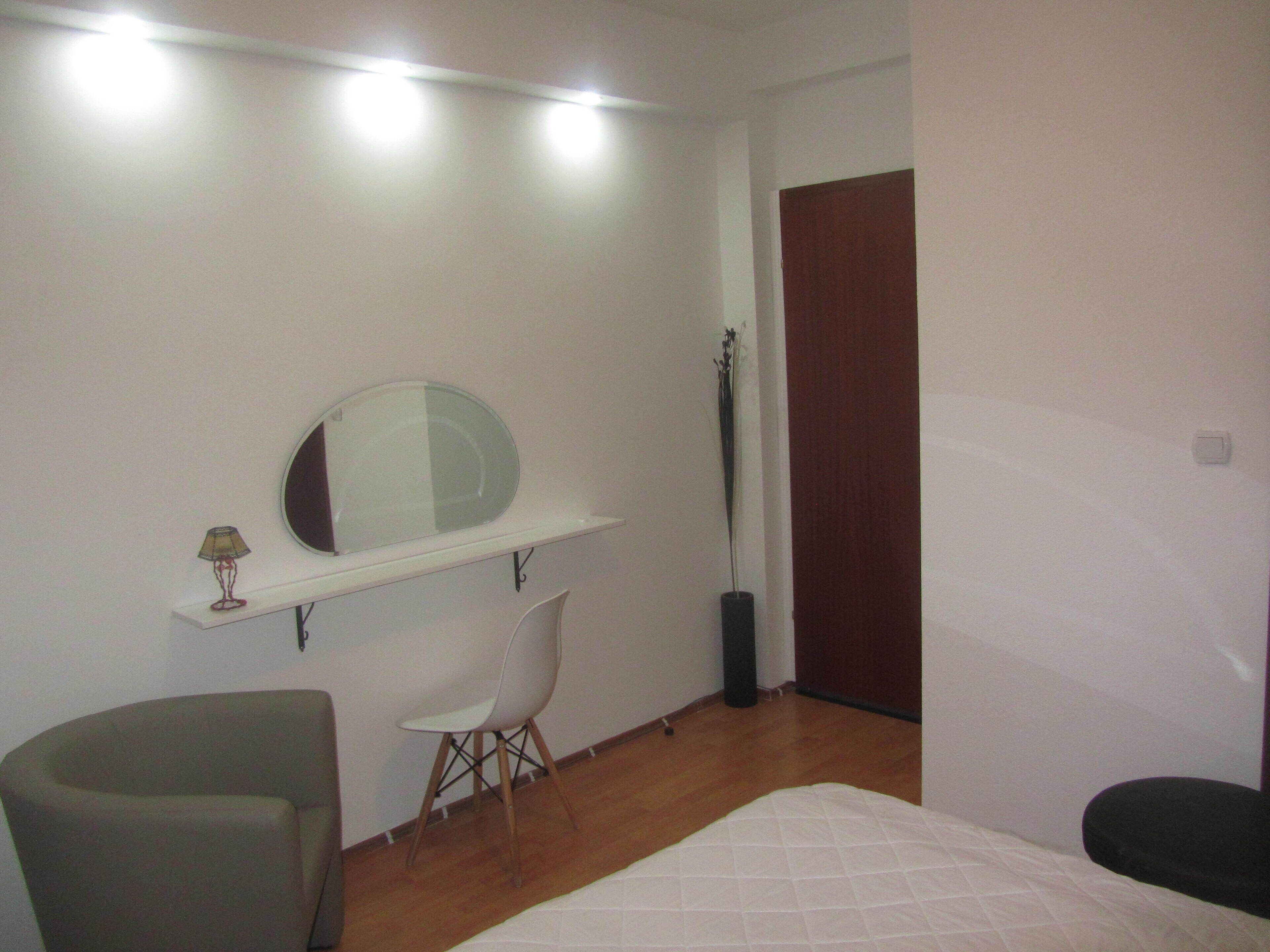 Un dormitorio con cama, una silla, un escritorio con espejo y una puerta.