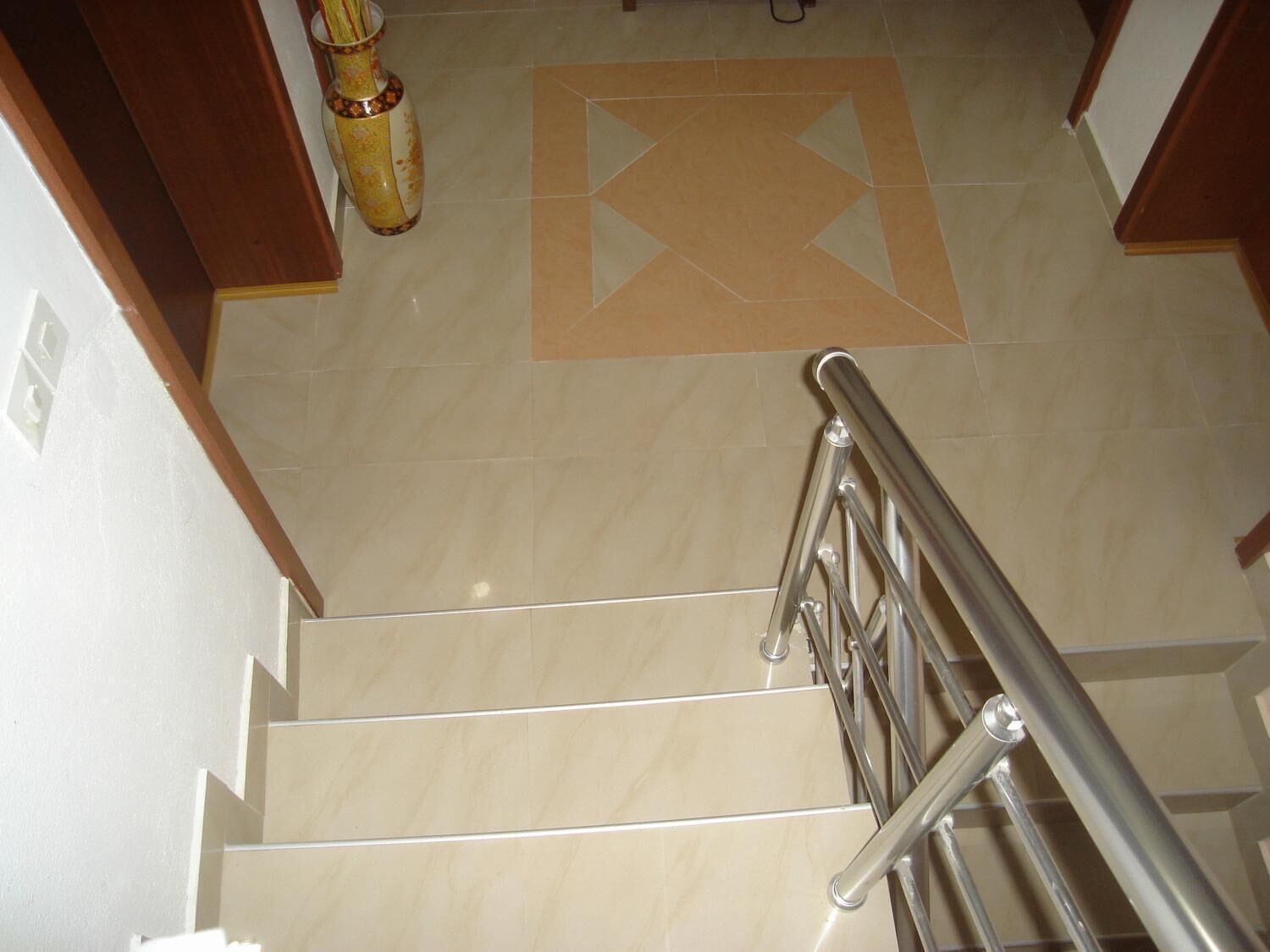 A staircase with a metal handrail, beige tiles, and a decorative tile pattern on the floor.