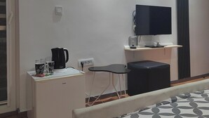 A hotel room with a bed, a desk with a coffee maker, a TV on a stand, and a window with blinds. - Villa Old Town (Ohrid)