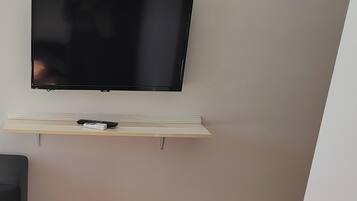 A flat-screen TV mounted on a wall above a wooden shelf with a remote control.