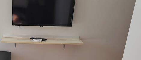 Un televisor de pantalla plana montado en la pared sobre un estante de madera, con un control remoto.
