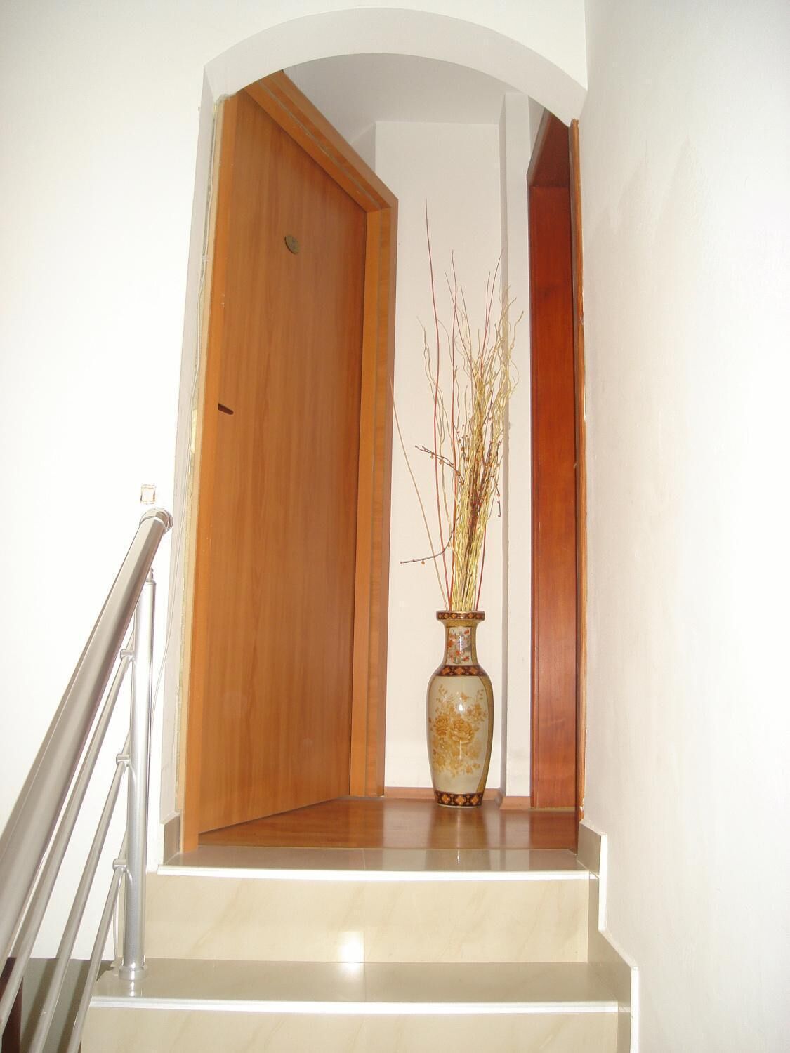 A staircase with a wooden door at the top and a vase with branches on the landing.