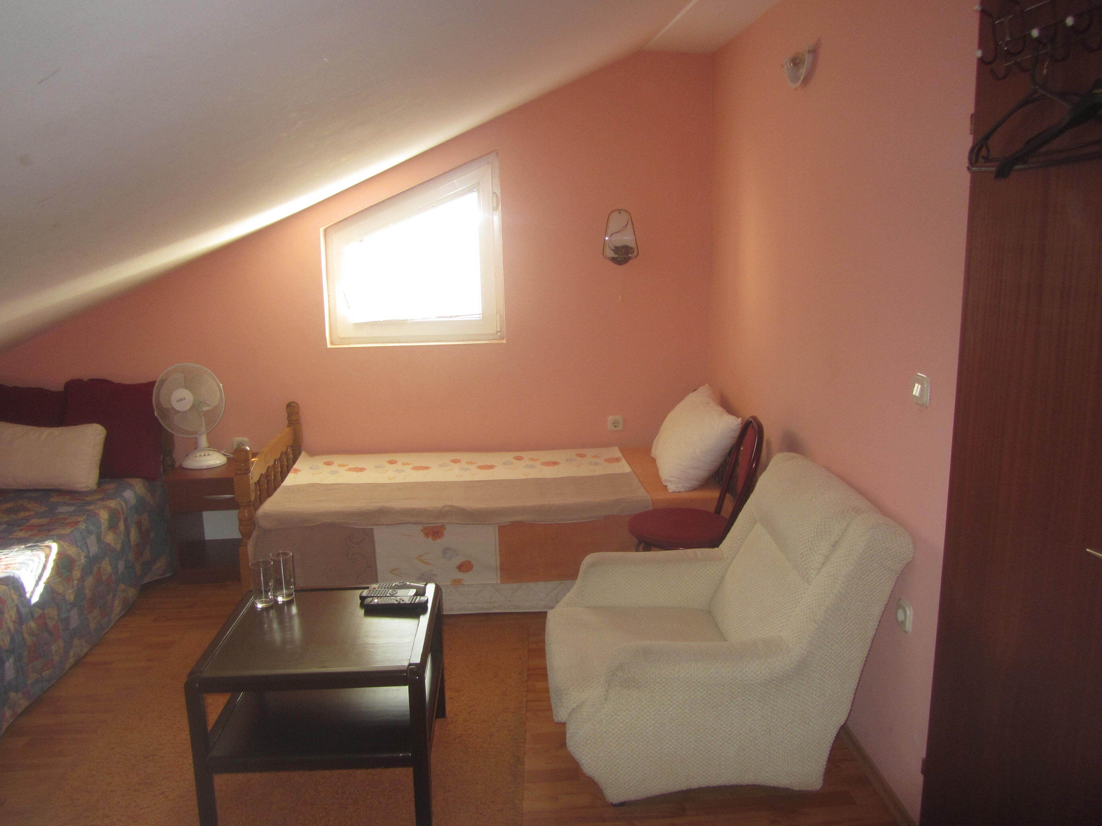 Um quarto pequeno e acolhedor com uma cama de solteiro, uma cadeira, uma mesa e uma janela.