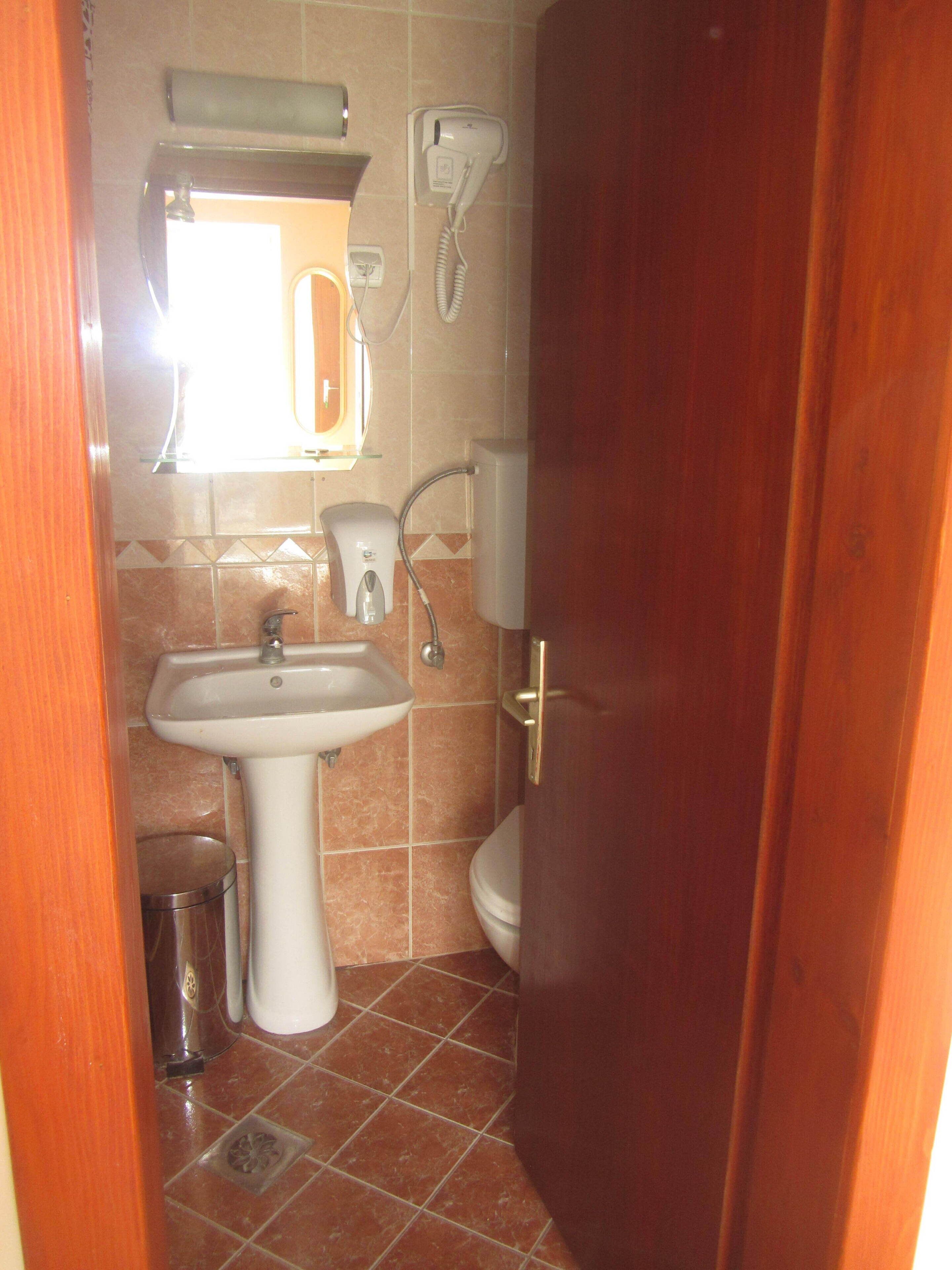 Un baño pequeño con lavamanos, inodoro y secador de pelo montado en la pared.