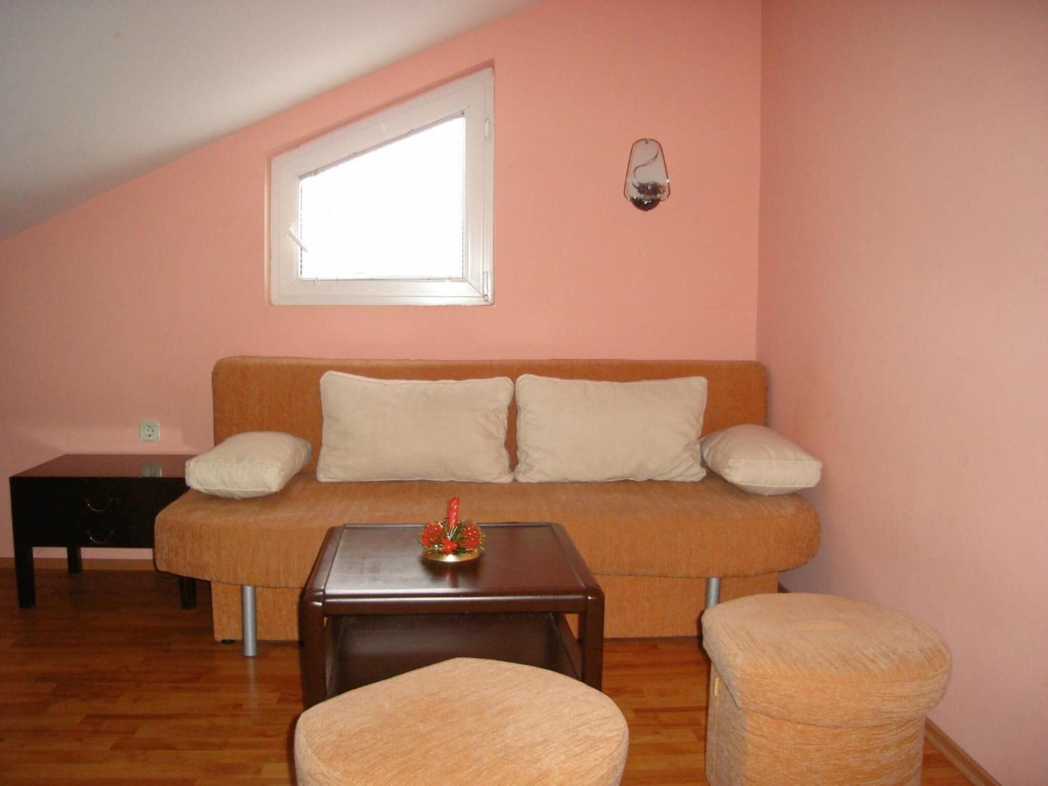 A cozy living room with a peach-colored wall, a brown sofa with two pillows, a small wooden table with a decorative item, and two round chairs.