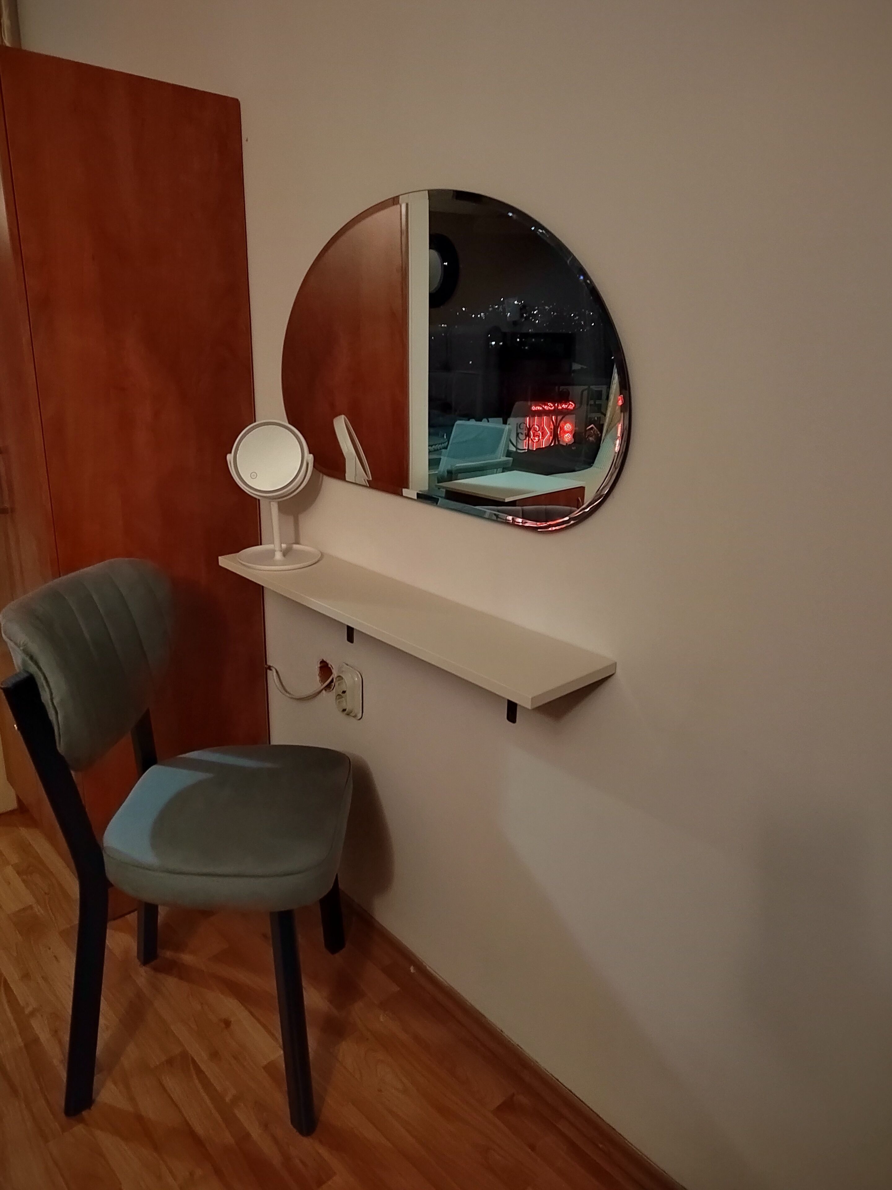 A corner desk with a round mirror, a chair, and a shelf.