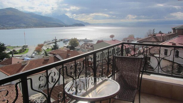 A balcony with a table and chairs, overlooking a lake with boats and buildings. - Villa Old Town (Ohrid)