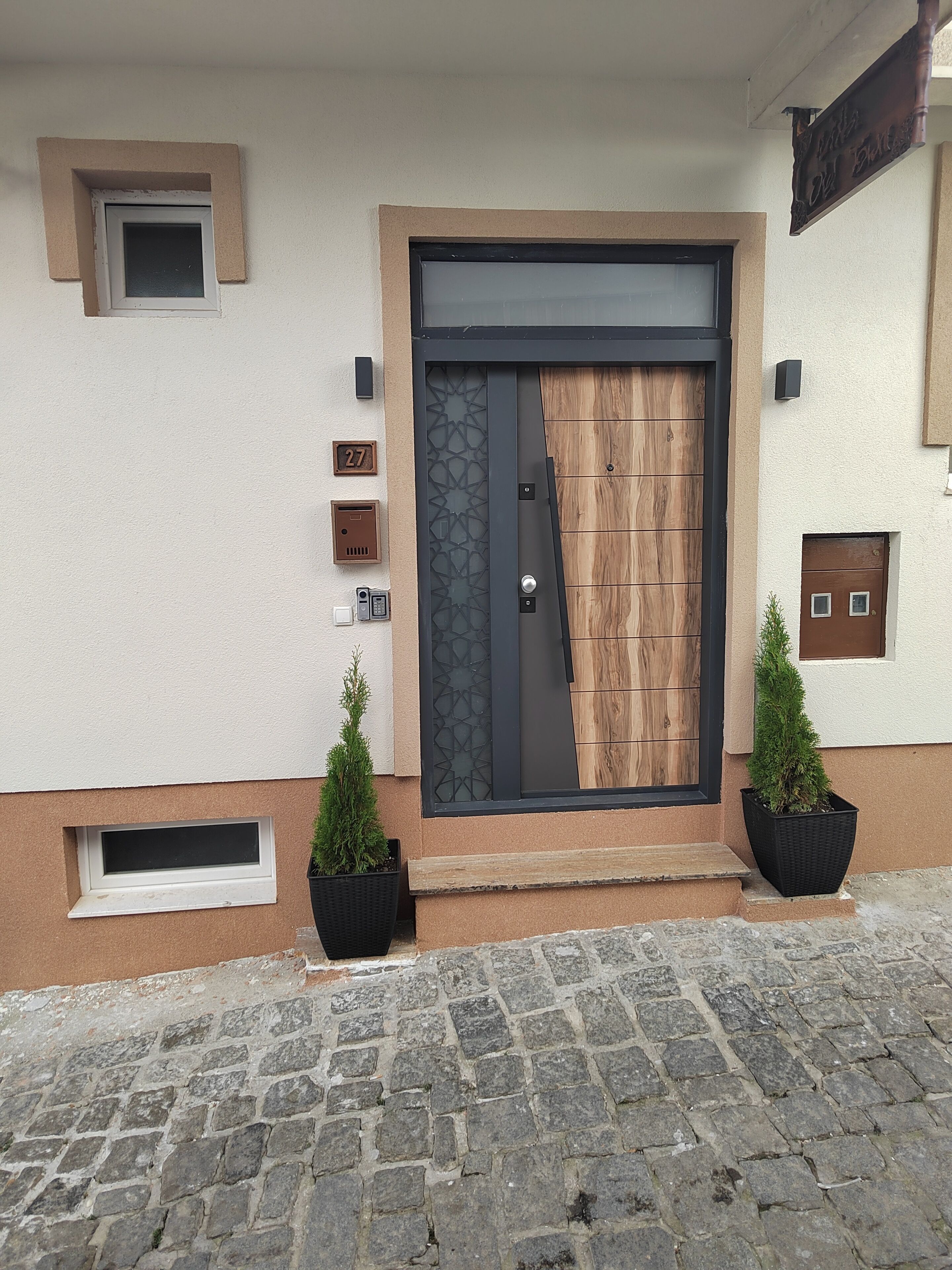 A building facade with a large wooden door, a small window, and a mailbox.
