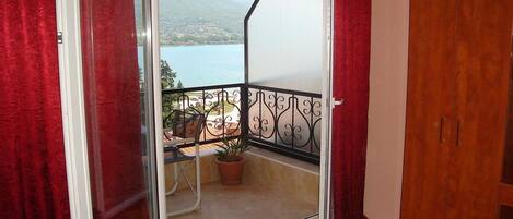 A balcony with a view of a lake and mountains, a wooden door, and a chair with a potted plant.