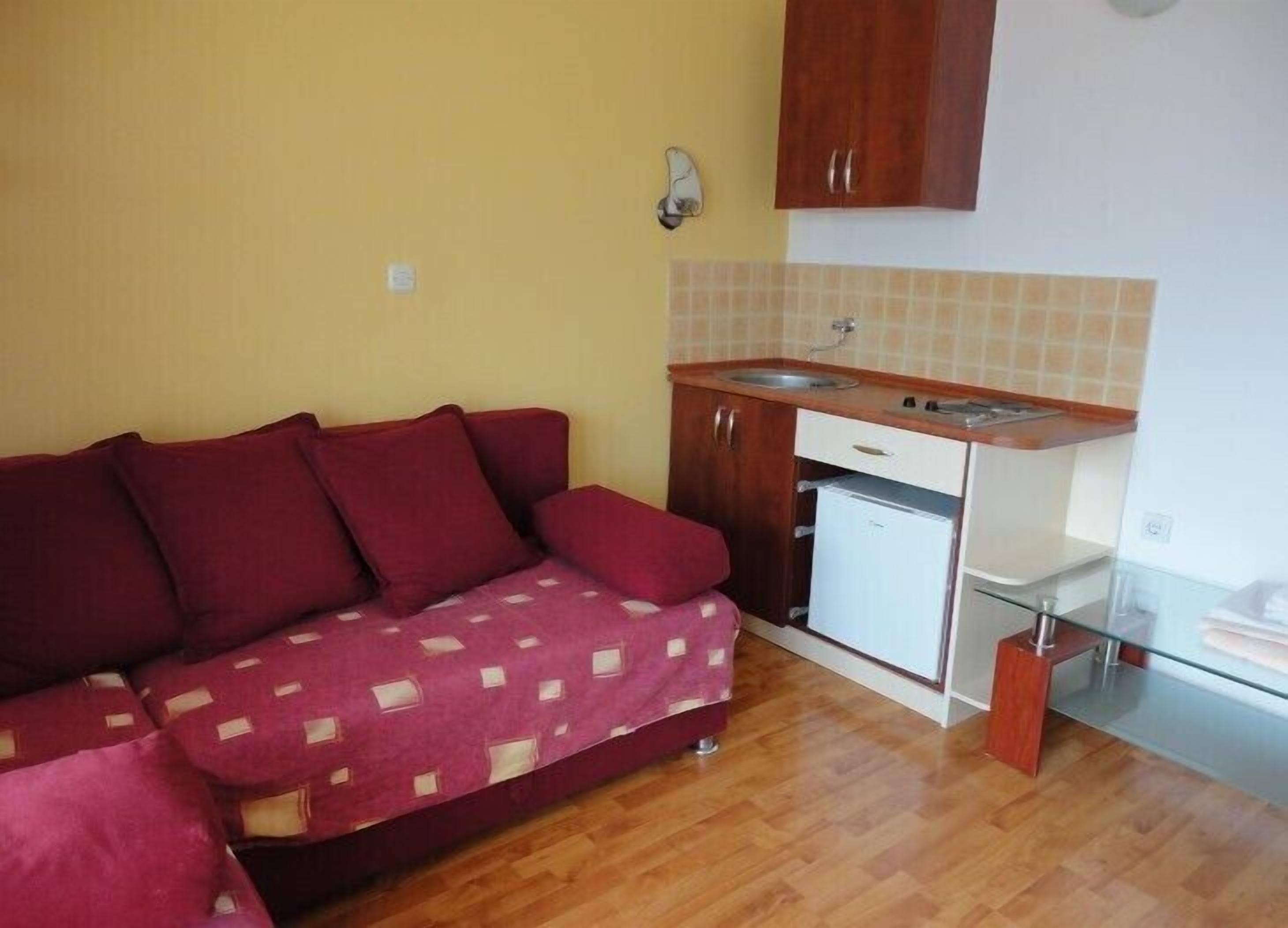 A compact living space with a sofa, a small kitchenette, and a glass table.