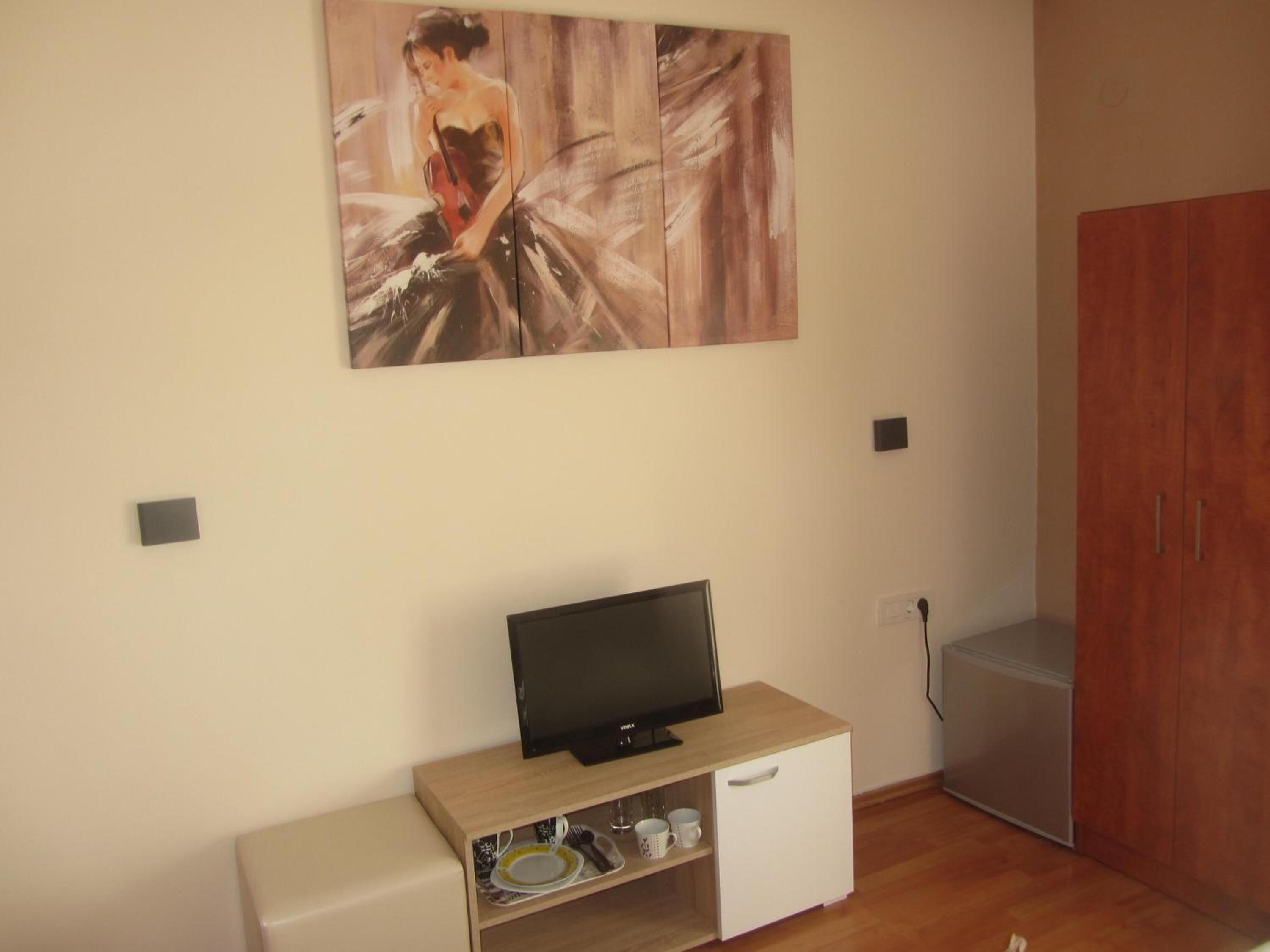 A room with a television on a wooden stand, a small cabinet with dishes, and a wardrobe.