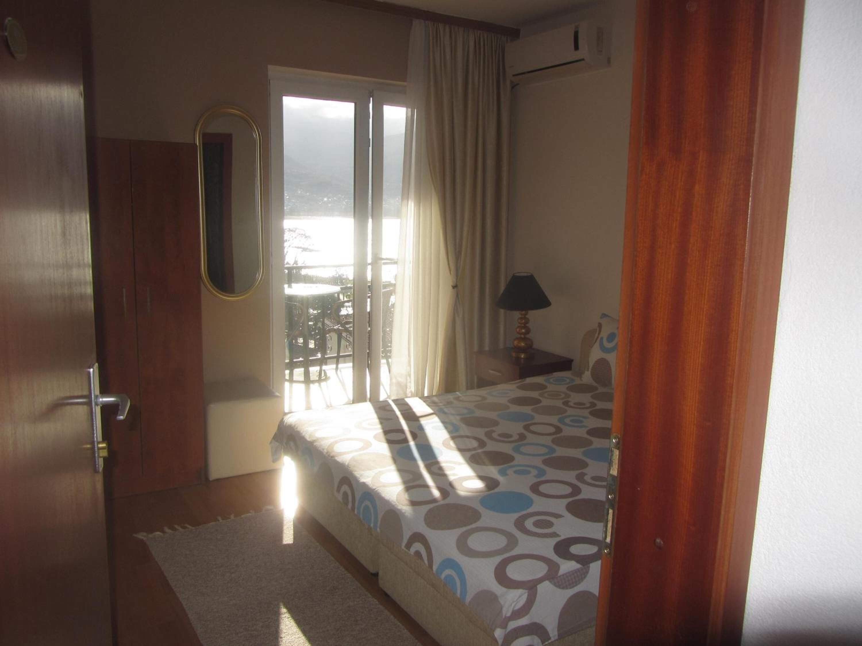 A hotel room with a bed, a small table with a lamp, a window with curtains, and a view of the outside.