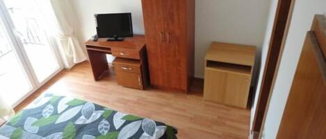 A room with a wooden desk, a television, a wardrobe, and a bed with a leaf-patterned bedspread.