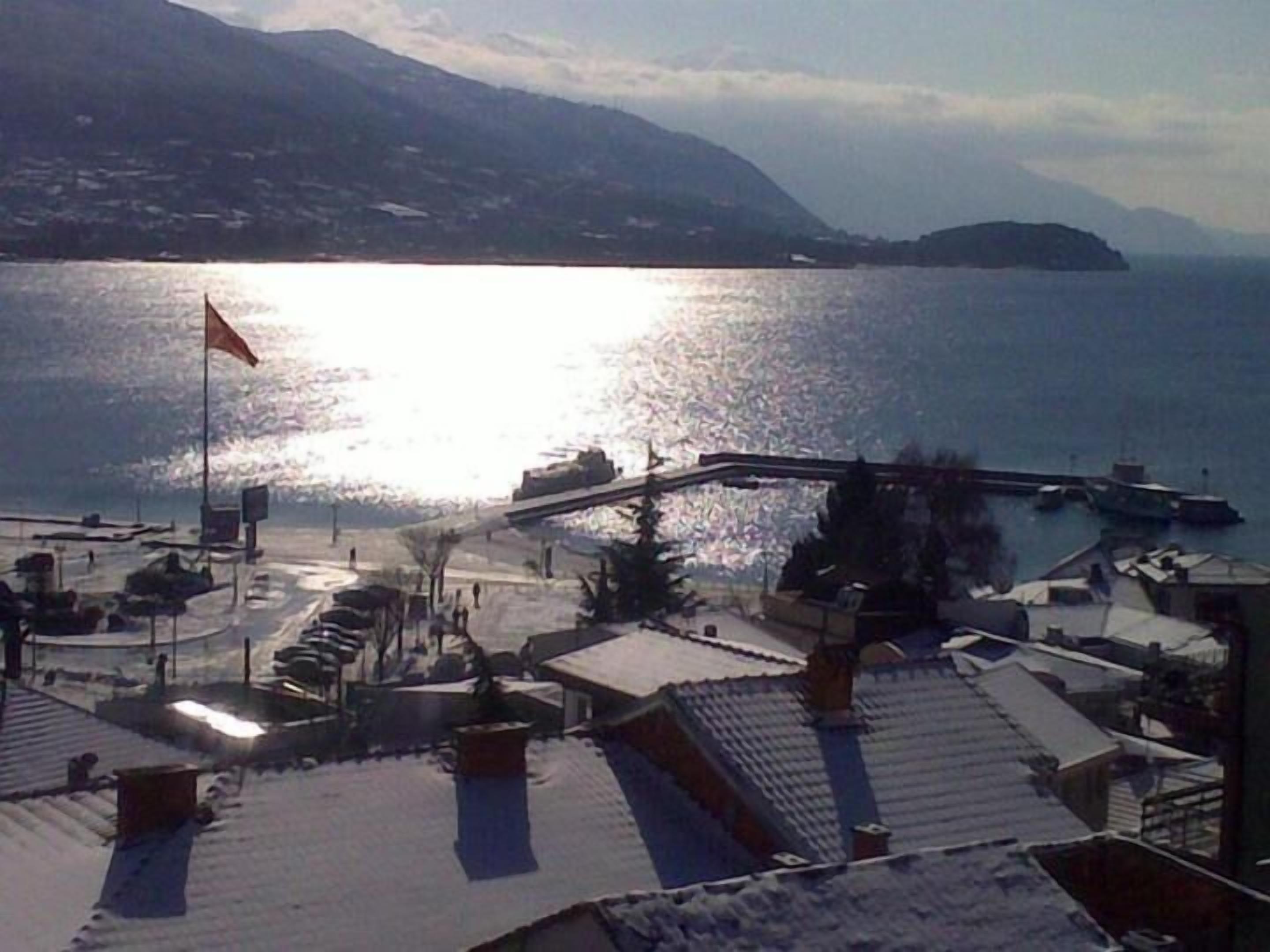A snowy landscape with a body of water, a bridge, and buildings in the background.
